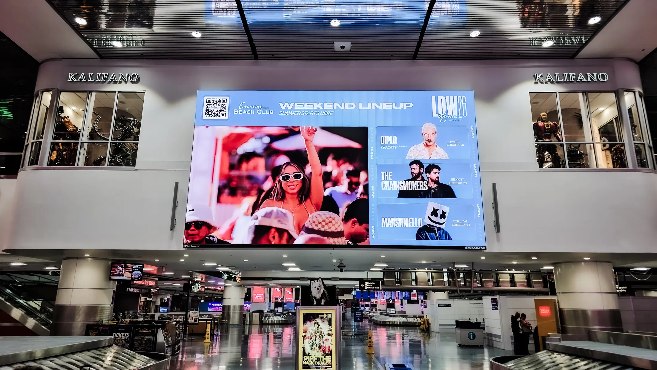 Wynn Nightlife weekend lineup on a large digital screen above an airport baggage claim, Las Vegas.